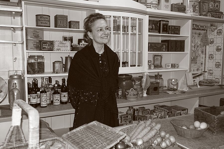 Schwarz-weiß Aufnahme eine Frau, die als Verkäuferin in einem Kolonialwarenladen hinter der Theke steht