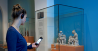 Frau steht mit Audioguide vor einer Vitrine im Museum
