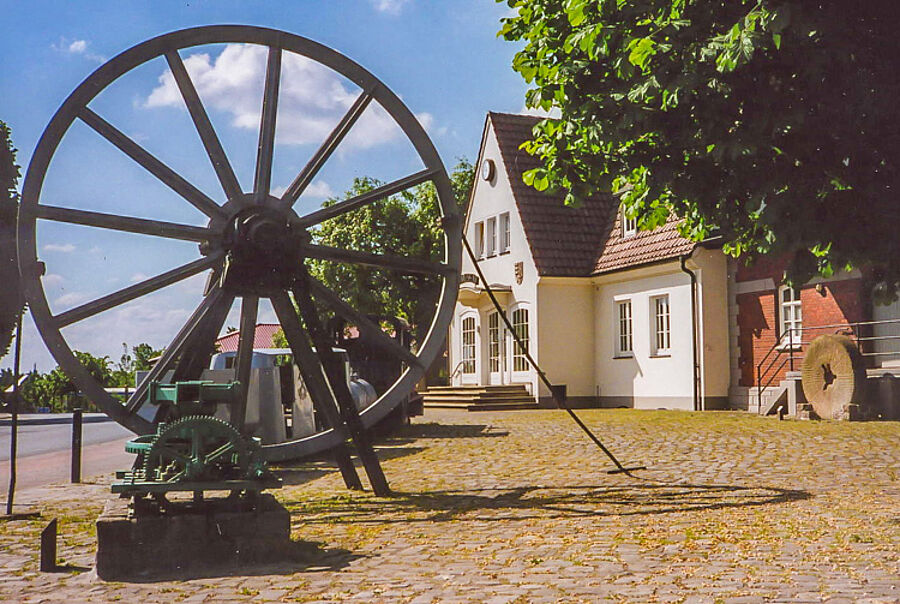 Rad des früheren Förderturms und Untertagezug als Zeugen des Dammer Eisenerzbergbaus, vorn ein Göpel, rechts ein Mühlstein