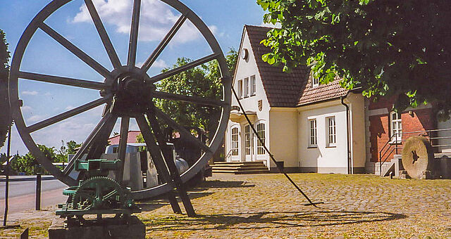 Rad des früheren Förderturms und Untertagezug als Zeugen des Dammer Eisenerzbergbaus, vorn ein Göpel, rechts ein Mühlstein